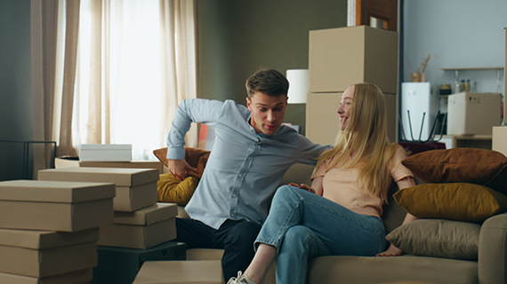 Zwei Personen sitzen auf einem Sofa in einem Raum voller Umzugskartons.